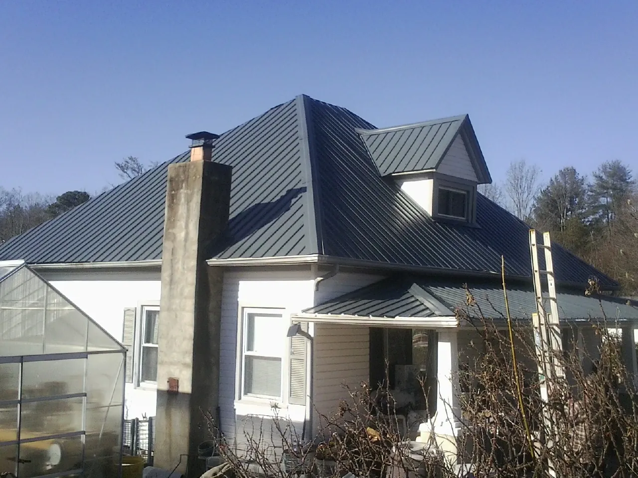 Dark blue standing seam metal roof on a white farmhouse with dormer — Slate & Tile Roof Repair by Roofing Brothers in Indian Wells
