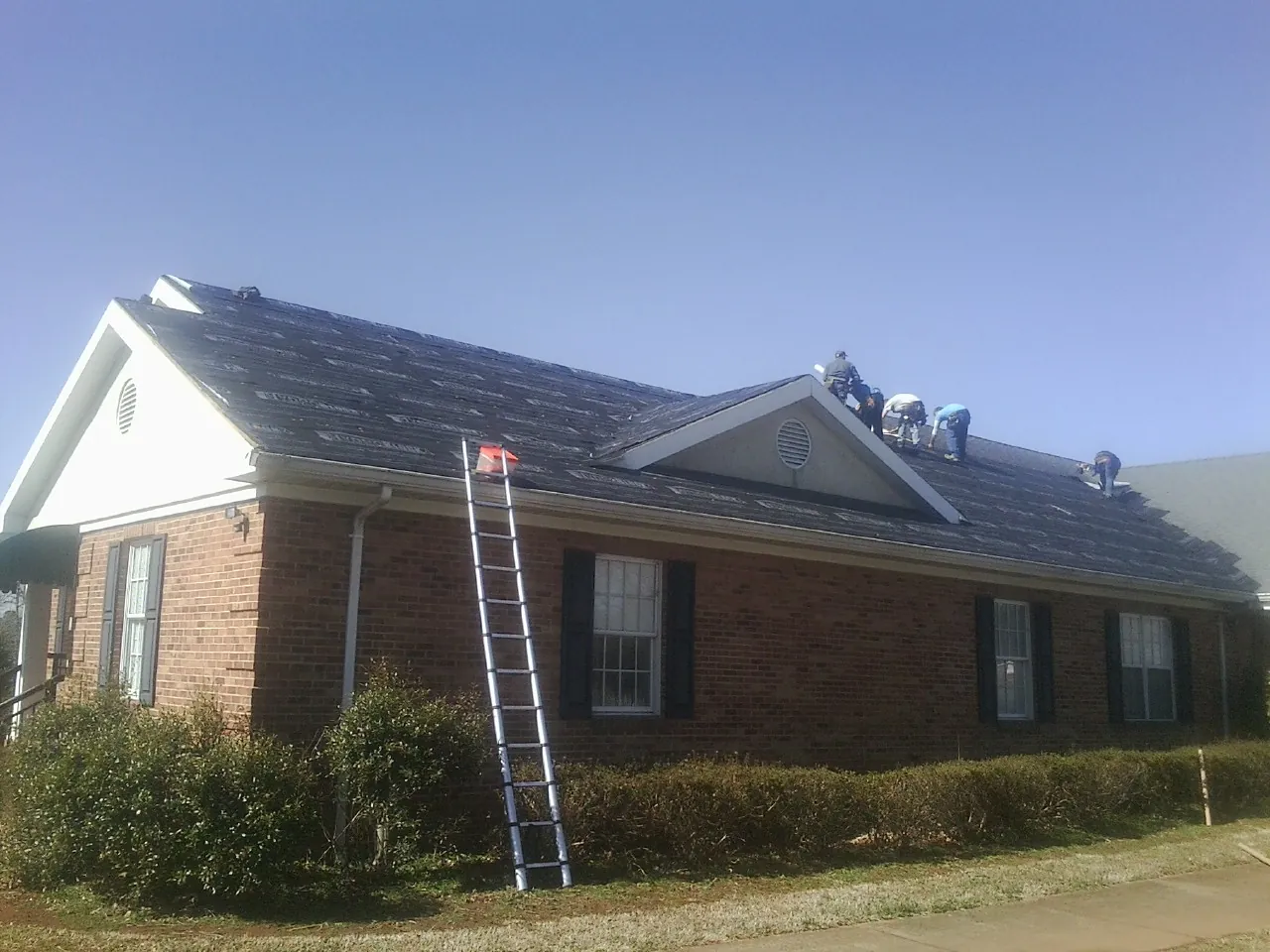 Crew tearing shingles off a brick ranch roof with a ladder set — Metal Roof Repair work by our crew in Indian Wells