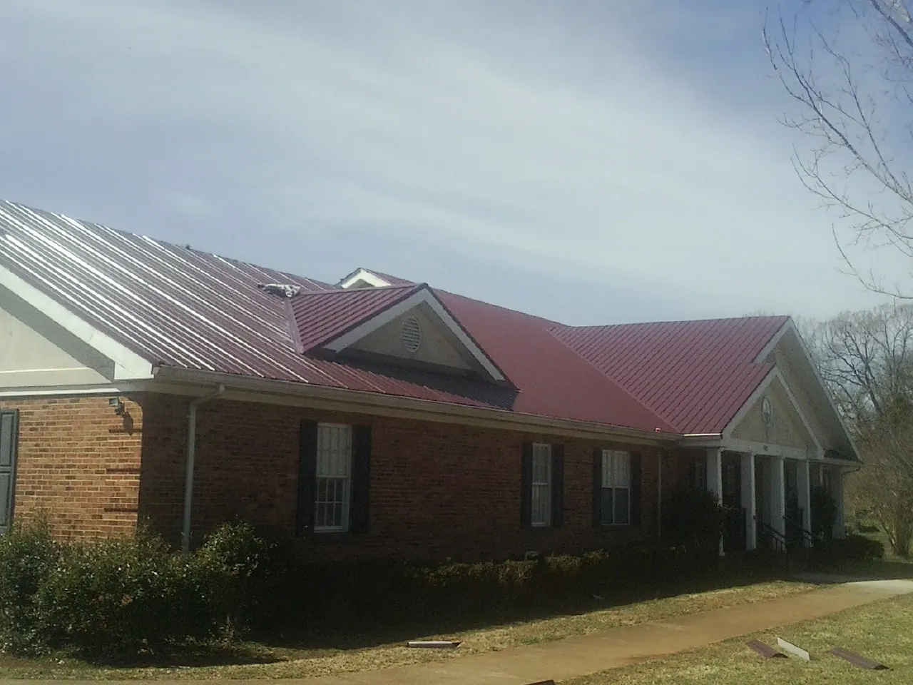 Red metal roof with gabled entries on a long brick building, from a Hail Damage Roof Repair job in Indian Wells
