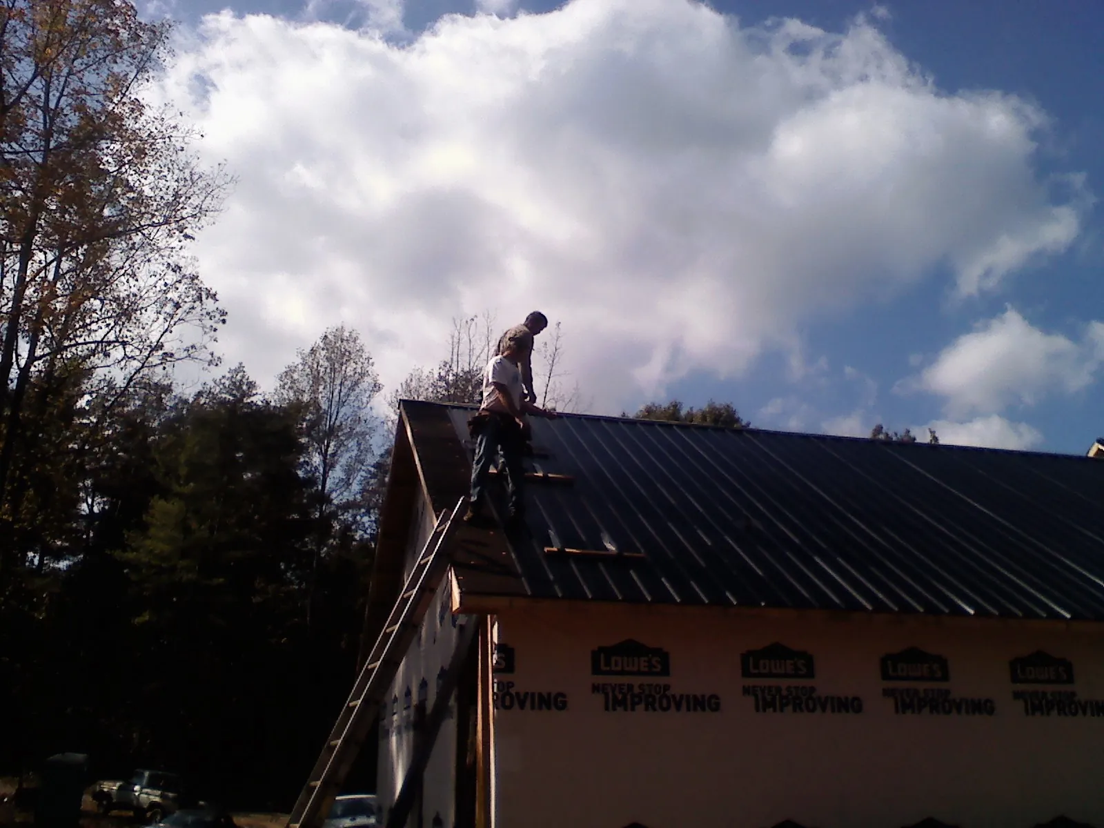 Roofer fastening dark metal panels high against a cloudy sky, from a Roof Inspection job in Indian Wells